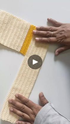 two hands are working on a knitted armband with an orange strip in the middle