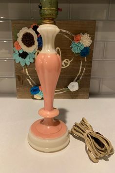 a pink vase sitting on top of a white table next to a string and flower decoration