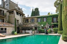 an outdoor swimming pool surrounded by hedges and stone buildings, with a woman standing in the middle