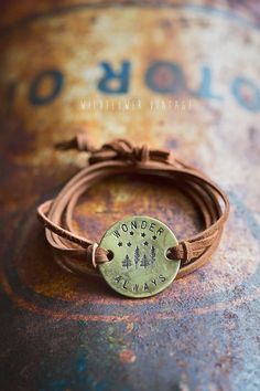 a brown leather bracelet with a brass disc on it and the words wildflower village