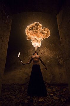 a woman in a black dress holding a lit up fire ball over her head and arms