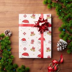 a christmas present wrapped in white paper with red ribbon and decorations around it on a wooden table