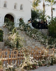 an outdoor ceremony setup with chairs and flowers on the steps leading up to the building