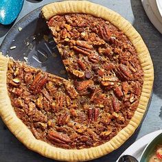 a pecan pie with one slice missing from it on a table next to plates and utensils