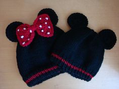 two crocheted hats with bows on them sitting on a wooden table, one is black and the other is red