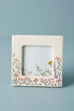 a white photo frame with an orange and blue flower design on the front, against a light blue background