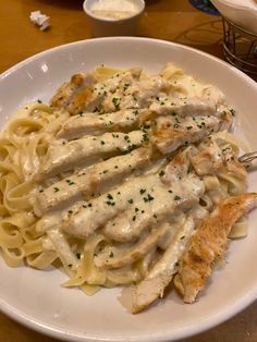 a white plate topped with pasta covered in sauce and chicken breast pieces on top of it