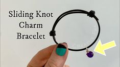 a person holding onto a black cord bracelet with a purple bead charm on it