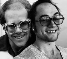 black and white photograph of two men with glasses on their heads smiling at the camera