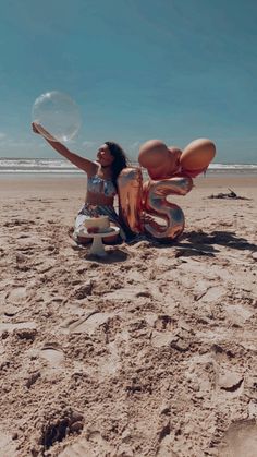 a woman sitting on the beach with her arms in the air while holding a bubble