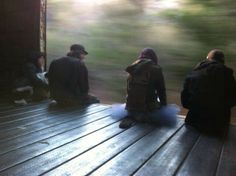 three people sitting on a wooden deck in front of a window looking at the woods