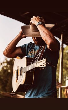 a man wearing a cowboy hat and holding a guitar in his right hand while standing under a tent