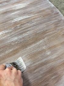 a person with a brush on top of a wooden table that is being stained white