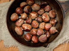 an iron skillet filled with chestnuts sitting on top of a wooden table next to a cloth