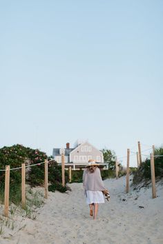 a woman walking down a sandy path towards the beach