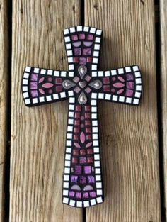 a cross that is on the side of a wooden fence with purple and white designs