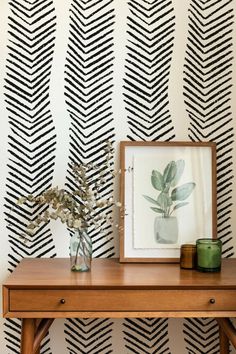 a wooden table topped with a vase filled with flowers next to a black and white wallpaper