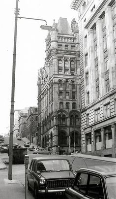 black and white photograph of cars parked on the side of a street in front of tall buildings