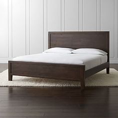 a bed sitting on top of a white rug next to a wooden headboard and foot board