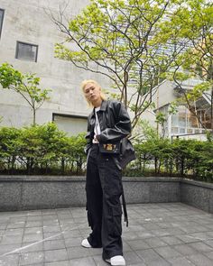 a woman standing in front of a building wearing black pants and a leather jacket with an embellished belt