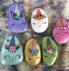 four painted rocks with unicorn faces and flowers on them, sitting on a carpeted surface