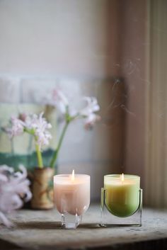 two candles sitting next to each other on top of a table with flowers in the background