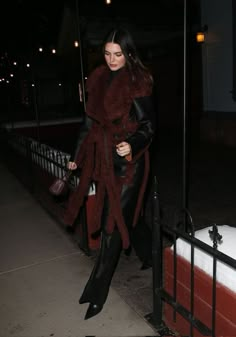 a woman walking down the street in black leather pants and a red scarf over her shoulders