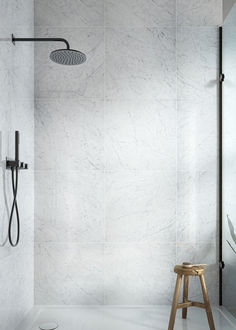 a white tiled bathroom with a stool and shower head