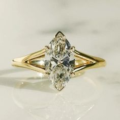 a yellow gold engagement ring with a pear shaped diamond in the center, on a white surface