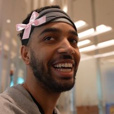 a man with a pink bow on his head smiles at the camera while wearing a gray shirt