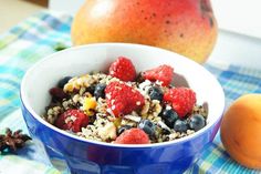 a blue bowl filled with cereal and fruit next to an orange on a tablecloth