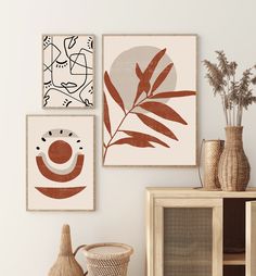 three framed art pieces hang on the wall above a wooden cabinet with vases and baskets