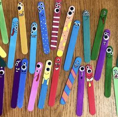 many different colored toothbrushes are lined up on a wooden table with faces painted on them