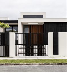 a modern house with black and white fences on the side of the street in front of it