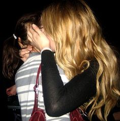 a woman with long blonde hair covering her face while standing next to a man in striped shirt