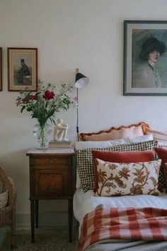 a bedroom with a bed, nightstand and pictures on the wall above it that have flowers in vases