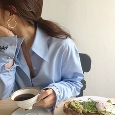 a woman sitting at a table with a cup of coffee in front of her face