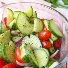 a glass bowl filled with cucumbers, tomatoes and onions on top of a pink towel