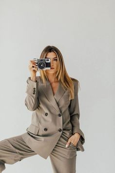 a woman in grey suit taking a photo with a camera while standing on one leg