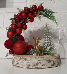 a christmas decoration with red balls and greenery on a white brick wall behind it is a gold deer figurine