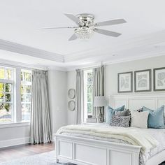 a white bed sitting in a bedroom on top of a hard wood floor next to two windows