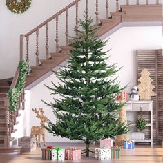 a christmas tree in front of a staircase with presents on the floor next to it