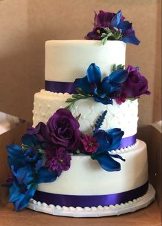 a three tiered wedding cake with purple and blue flowers