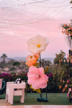 large paper flowers on display in front of an outdoor setting at dusk with string lights