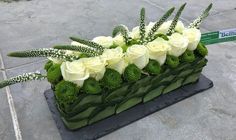 a bouquet of white roses and green leaves on a black stand with a sign in the background