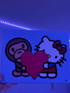 someone holding up a hello kitty painting in front of a blue wall with lights on it