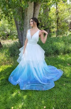 a woman in a blue and white dress standing next to a tree with her hands on her hips