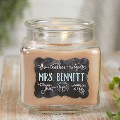 a candle is sitting on a table with some plants in the background and a chalkboard sign that says, mrs bennett