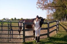 a woman standing next to a brown horse on top of a lush green field near a wooden fence