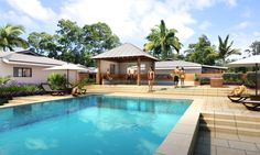 an outdoor swimming pool with lounge chairs and umbrellas next to it, surrounded by palm trees